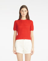 A woman faces forward against a white background, wearing the Draper James Short Sleeve Pointelle Sweater in red with white shorts.