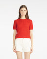 A woman faces forward against a white background, wearing the Draper James Short Sleeve Pointelle Sweater in red with white shorts.