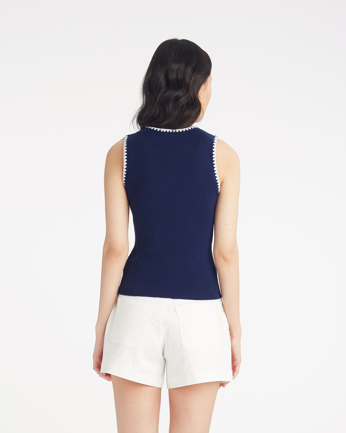 A person stands facing away, wearing the Draper James Sweater Tank in navy with white trim and white shorts against a plain white background.