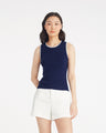 A woman stands against a plain background wearing the Draper James Sweater Tank in navy with white trim, paired with white shorts.