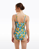 A woman faces away in the Draper James Lemon Blossom Bandeau One Piece—a blue swimsuit featuring a lemon and leaf print, offering stylish UPF 50+ sun protection.