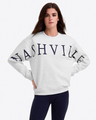 A woman wears the Draper James Nashville Crewneck Sweatshirt in light gray with bold "NASHVILLE" text, paired with navy leggings. This cozy cotton sweatshirt is perfect for country music fans.