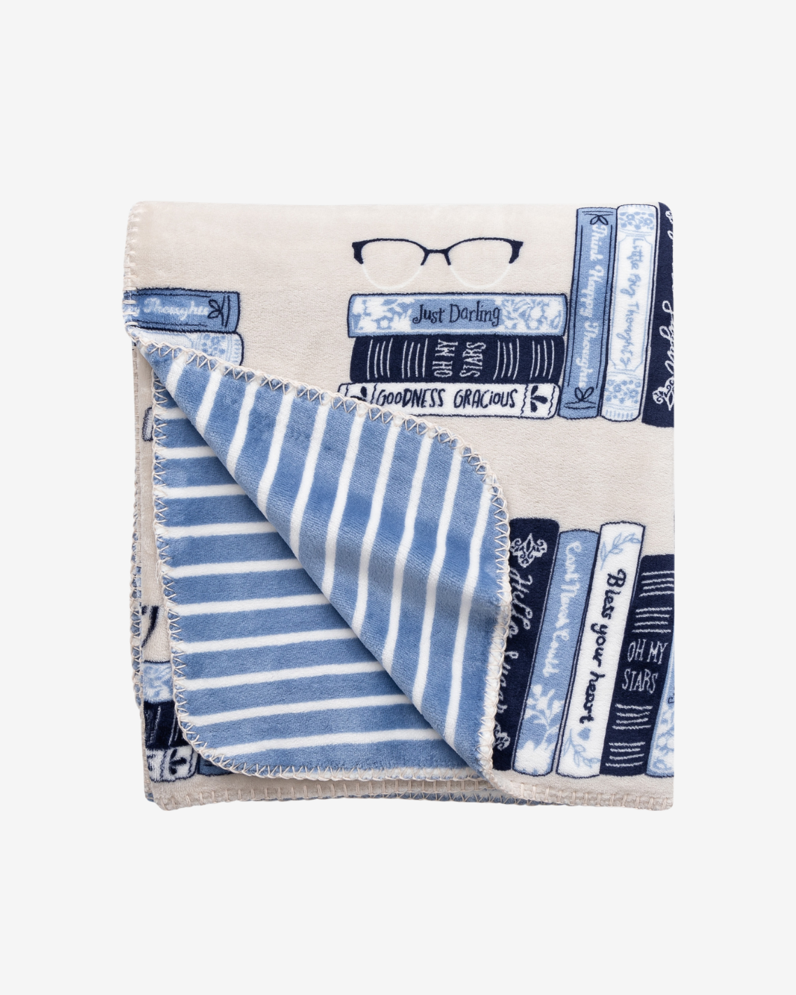 A folded cream-colored scarf featuring a book-themed print with blue and navy book spines, a pair of glasses, and a striped reverse side, displayed on a clean white background.