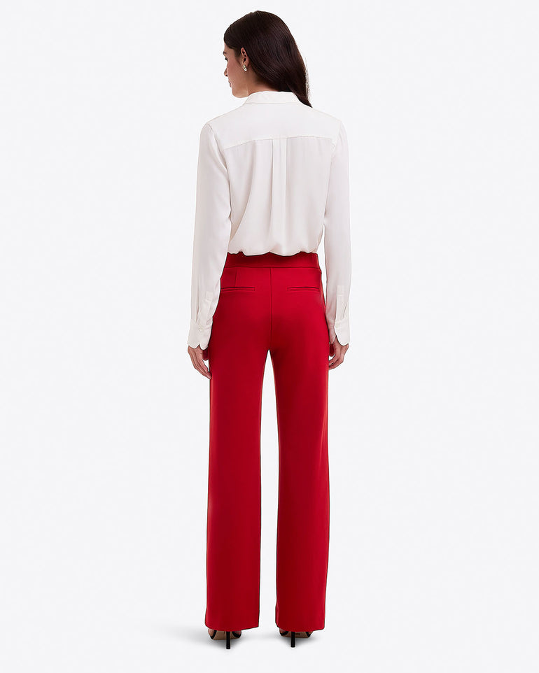 A woman faces away against a white background, wearing Draper James Flare Pants in Ponte in a lipstick shade, paired with a long-sleeve white blouse and black heels.
