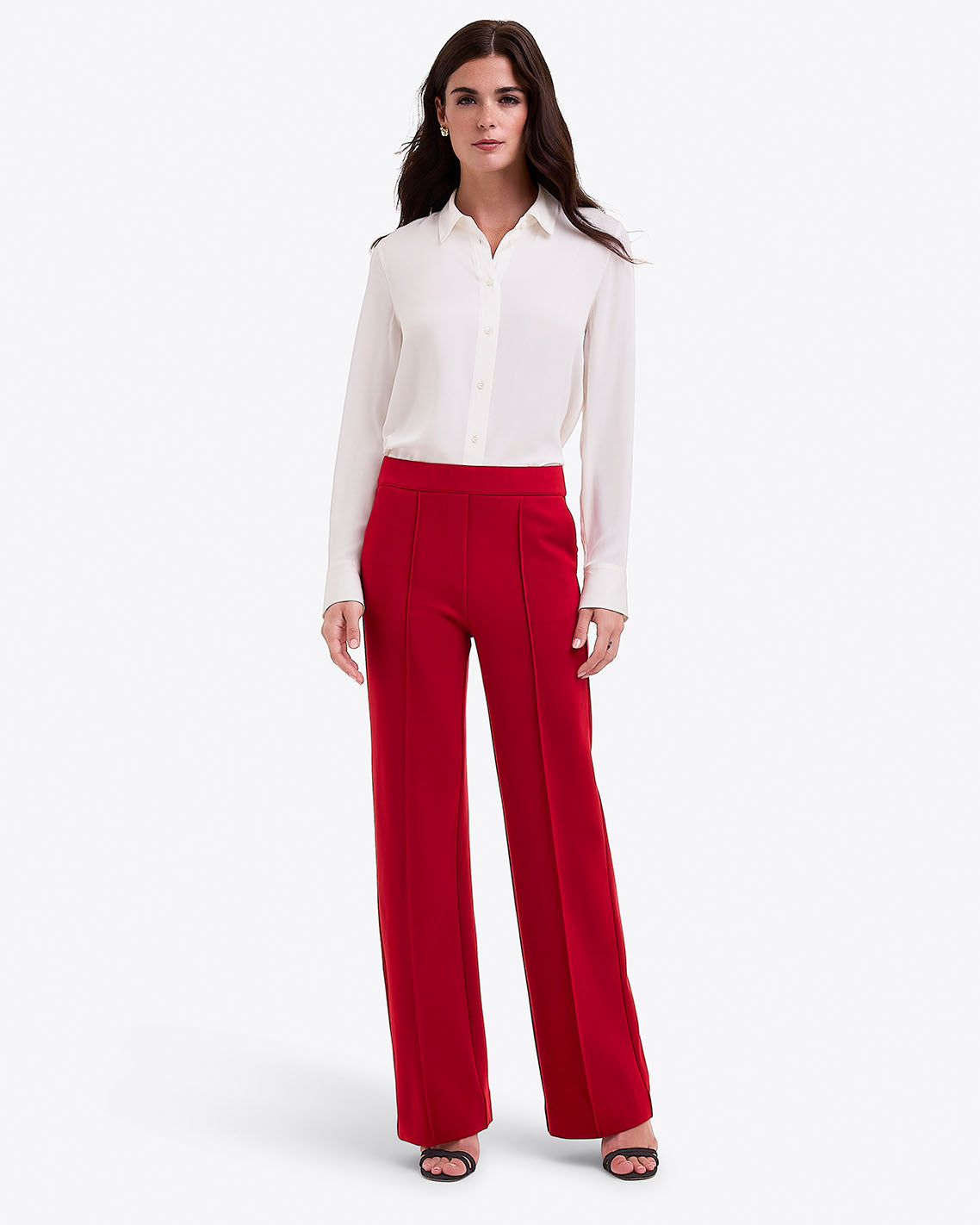 A woman stands against a white background wearing a white blouse, Draper James Flare Pants in Ponte in lipstick, and black open-toe heels.