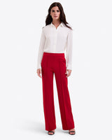 A woman stands against a white background wearing a white blouse, Draper James Flare Pants in Ponte in lipstick, and black open-toe heels.
