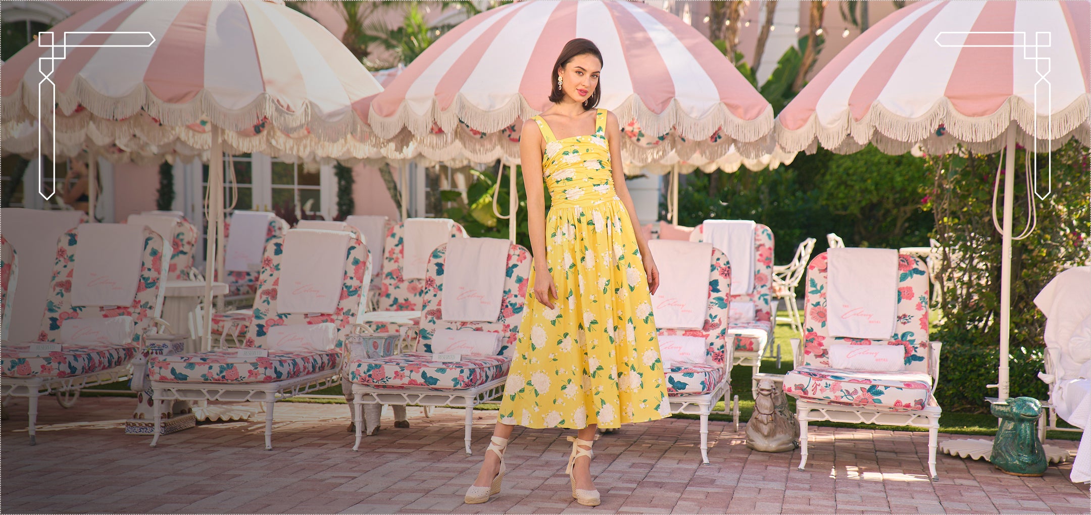 Woman in a yellow dress standing under a striped umbrella with floral chairs in the background