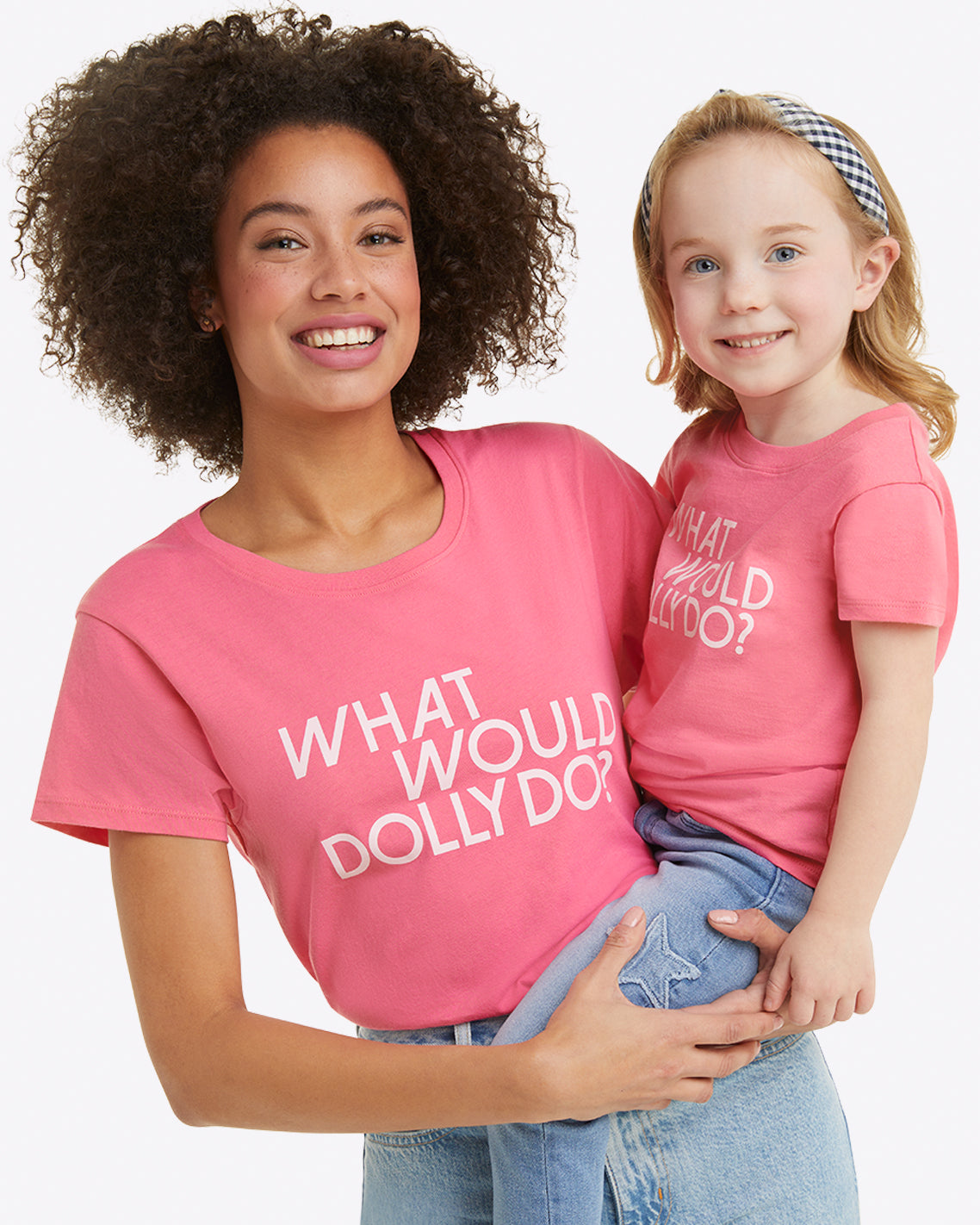 A woman cradles a child, both wearing Draper James' soft jersey cotton pink shirts with the words "What Would Dolly Do?" The child's shirt is the Kids WWDD Pink T-Shirt.