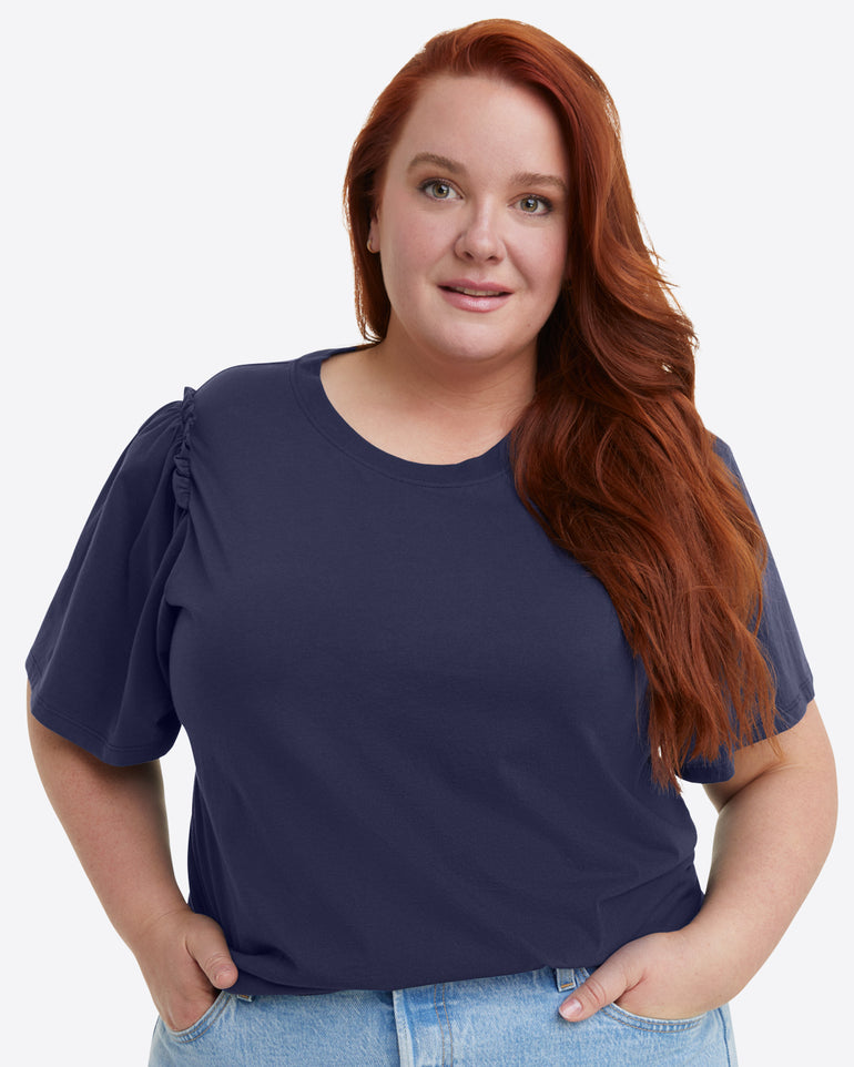 A person with long red hair wears a Short Sleeve Easy Knit Top in Navy from Draper James, made of 100% Pima Cotton, paired with jeans and standing against a plain white background.