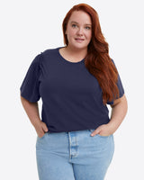 A person with long red hair is wearing a Draper James Short Sleeve Easy Knit Top in Navy made from 100% Pima Cotton, paired with light blue jeans, against a plain background.